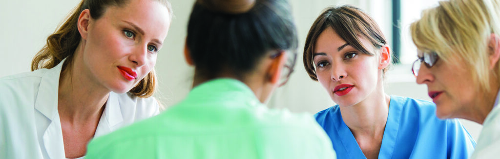 A photo of multi-ethnic medical team discussing at hospital. Female professionals are in meeting. Staff is in uniform.